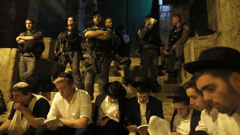 Los policías de frontera mantienen la guardia mientras los fieles oran durante el Tisha B’Av ayunando en una puerta que conduce al edificio del Monte del Templo de la Ciudad Vieja de Jerusalén el 31 de julio de 2017. (AFP Photo / Menahem Kahana)