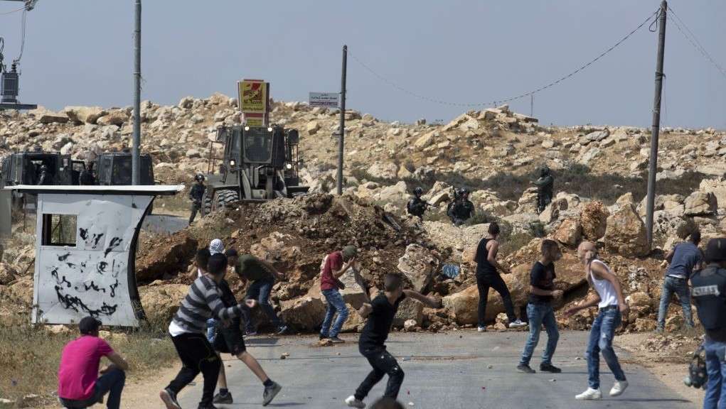 Turbas islámicas lanzan piedras a los soldados israelíes en la aldea de Kobar, mientras una excavadora del ejército cierra la carretera principal hacia la zona durante una operación para preparar la casa de un terrorista para la demolición el 22 de julio de 2017. (AP Photo / Nasser Nasser)