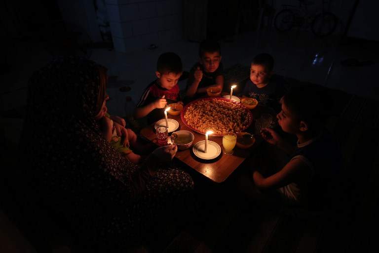 Una familia árabe come cena a la luz de las velas en su casa improvisada en  Rafah, en el sur de la Franja de Gaza, durante un corte de energía el 11 de junio de 2017. (AFP / SAIDA KHATIB)