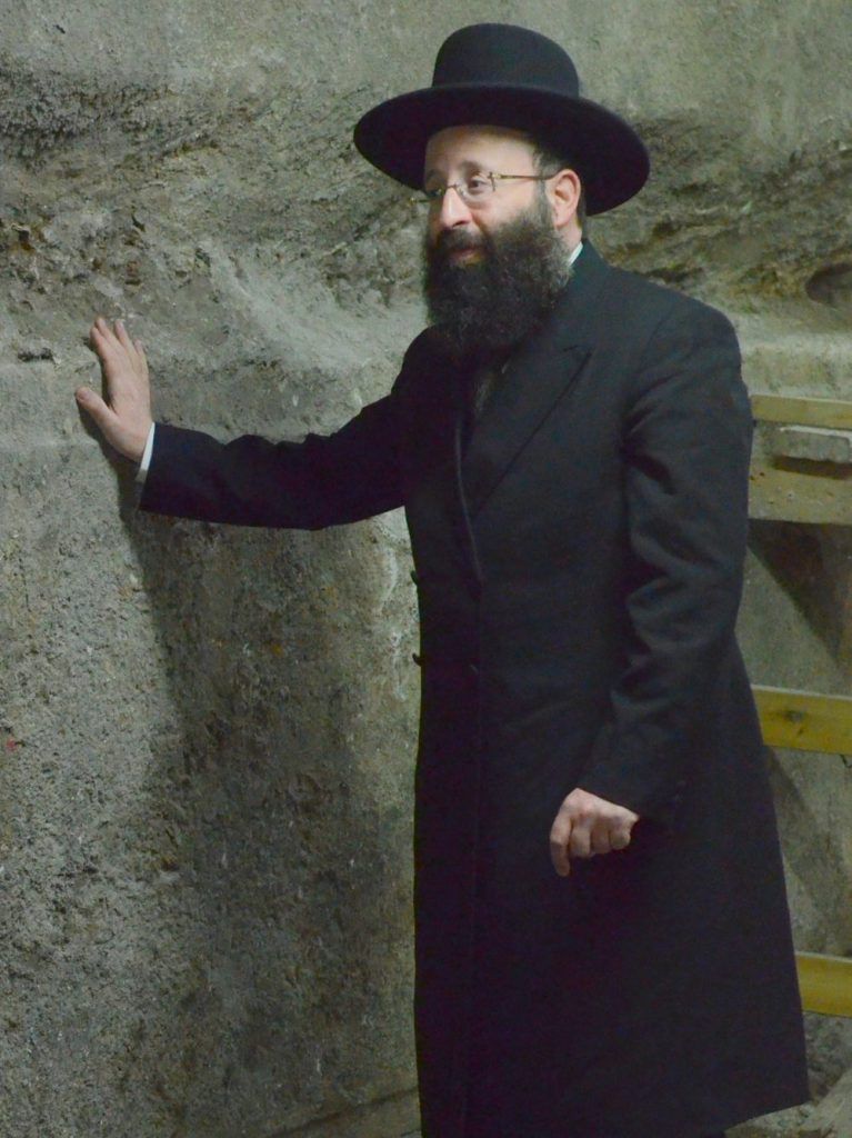 El rabino Shmuel Rabinovitch, el rabino del Muro Occidental y los lugares sagrados, toca una de las piedras del Muro Occidental descubiertas en la excavación bajo el Arco de Wilson en la Ciudad Vieja de Jerusalén. (Yaniv Berman, cortesía de la Autoridad de Antigüedades de Israel)