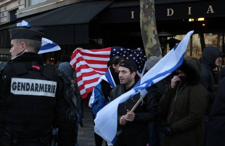 Un gendarme observa mientras un hombre ondea una bandera israelí y otro agita una bandera estadounidense mientras observa a los manifestantes que participan en una protesta anti-Israel en París el 9 de diciembre de 2017, contra el reconocimiento del presidente estadounidense Donald Trump de Jerusalén como la capital de Israel . (AFP / Zakaria Abdelkafi)