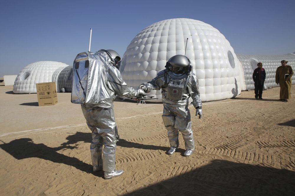 El astronauta analógico João Lousada, centro, le entrega a su colega Kartik Kumar un dron mientras dos hombres omaníes miran frente al campamento base de simulación de Marte en el desierto de Dhofar en Omán, el 7 de febrero de 2018. (AP Photo / Sam McNeil)