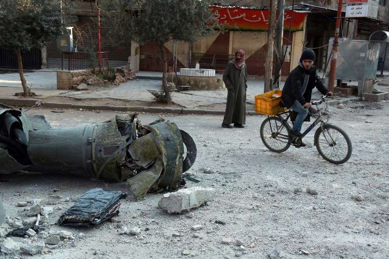 Hombres sirios caminan junto a los restos de un cohete en la ciudad de Douma, en la sitiada región oriental de Ghouta, en las afueras de la capital, Damasco, tras los ataques aéreos de las fuerzas del régimen en la zona el 23 de febrero de 2018. (AFP PHOTO / HAMZA AL-AJWEH)