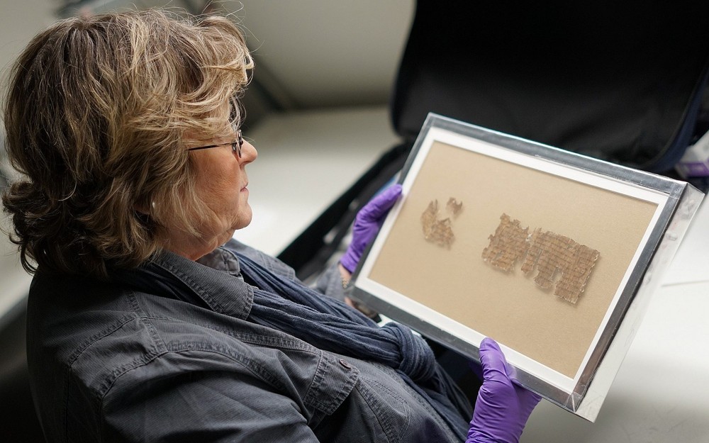 La conservadora de la Autoridad de Antigüedades de Israel Tatiana Treiger sostiene un fragmento del pergamino Tohorot, en exhibición pública por primera vez en el Museo de Naturaleza y Ciencia de Denver. (Yoli Shwartz, Autoridad de Antigüedades de Israel)