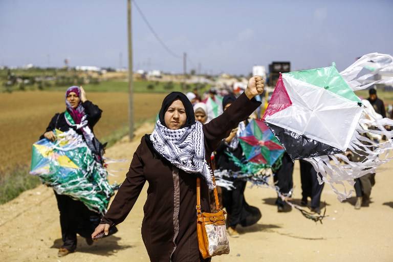 Mujeres árabes palestinas vuelan cometas marcadas con los colores de la bandera de la revuelta árabe durante una manifestación antes del Día de la Tierra, en una ciudad carpa a lo largo de la frontera con Israel al este de la ciudad de Gaza el 29 de marzo de 2018. (AFP PHOTO / MOHAMMED ABED)