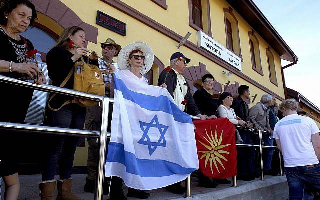 La gente sostiene la bandera israelí y la antigua Macedonia cuando participan en la conmemoración de las víctimas del Holocausto, en la estación de trenes de Bitola, en el sur de Macedonia, el 11 de marzo de 2018. (AP Photo / Boris Grdanoski)