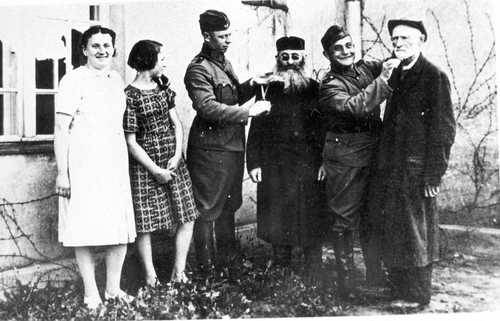 Praszka (Praschkau - Wartheland): policías alemanes cortan las barbas a dos judíos observantes. Junto a ellos dos chicas polacas ven la escena y se divierten. Yad Vashem, Jerusalén