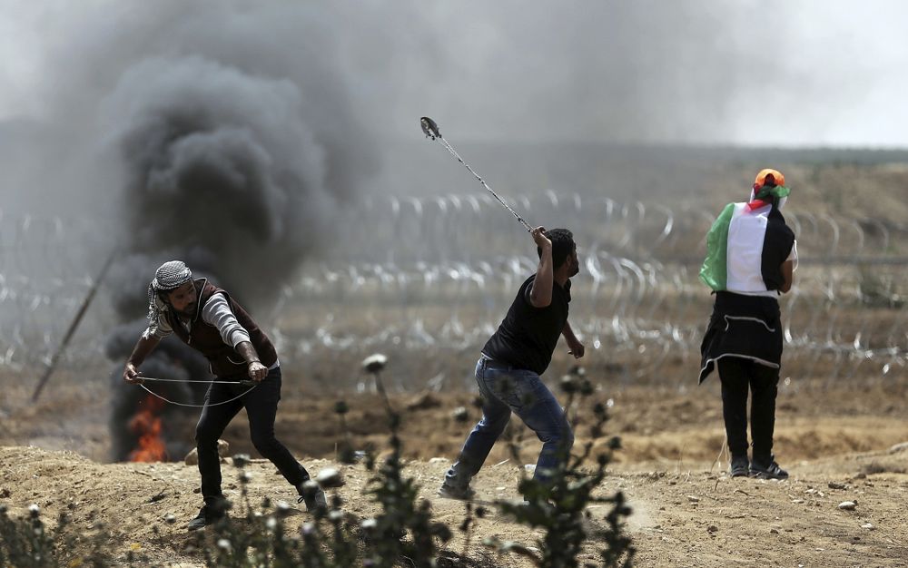 Los islamistas palestinos lanzan piedras contra las tropas israelíes en la frontera de la Franja de Gaza con Israel, el viernes 13 de abril de 2018. (AP Photo / Khalil Hamra)