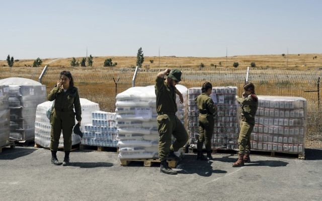 Los soldados de las FDI se encuentran junto a los suministros de alimentos que se preparan como ayuda humanitaria para los sirios afectados por la guerra civil en su país, el 19 de julio de 2017. (AFP / Menahem Kahana)