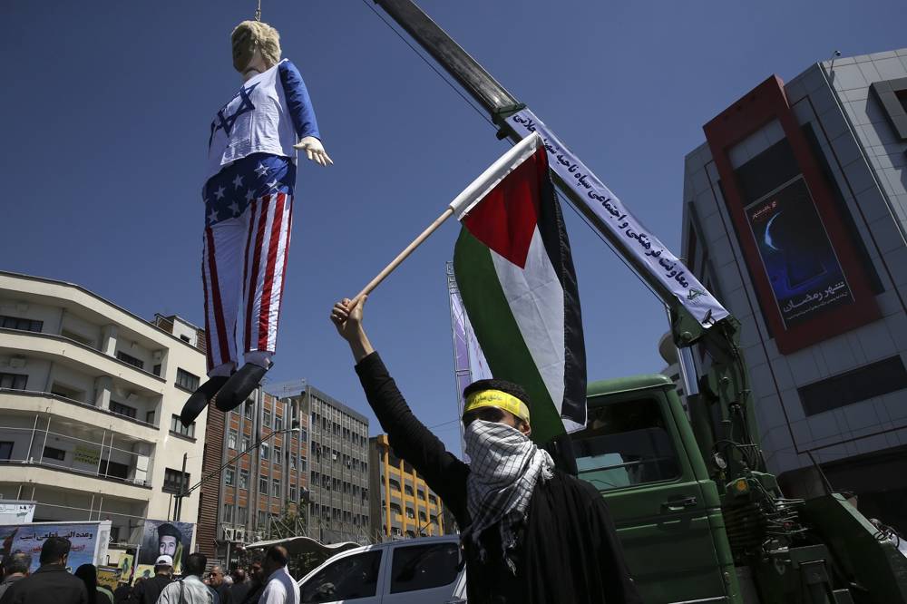 Un manifestante iraní sostiene una bandera de la Autoridad Palestina frente a una efigie del presidente estadounidense Donald Trump colgada de una grúa en la manifestación anual en Teherán contra el gobierno israelí, Irán, el viernes 8 de junio de 2018 (AP Photo / Vahid Salemi)