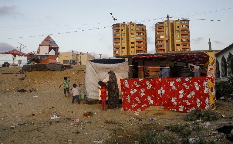 Noor, la esposa de 33 años de Hani al-Laham, empleada del gobierno de la Autoridad Palestina con sede en Ramallah, se encuentra con sus hijos frente a su choza cerca de la playa en la ciudad de Gaza el 4 de junio de 2018. (AFP Photo / Mohammed Abed)