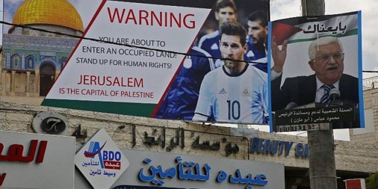 Este 5 de junio de 2018, la imagen muestra un cartel erigido en la ciudad cisjordana de Hebrón llamando a boicotear a la estrella de fútbol Lionel Messi (l) junto a un retrato del presidente de la Autoridad Palestina Mahmoud Abbas