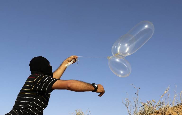 Un islamista palestino enmascarado lanza un globo cargado con materiales inflamables hacia Israel, al este de Rafah en el sur de la Franja de Gaza el 17 de junio de 2018. (AFP PHOTO / SAID KHATIB)