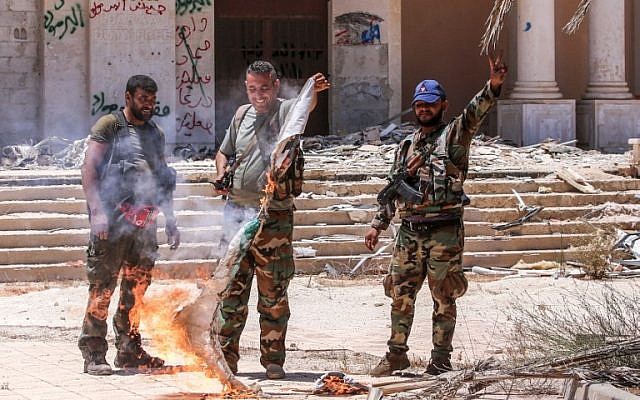 Soldados del gobierno sirio queman una bandera de oposición mientras muestran el gesto de victoria en el cruce fronterizo de Nassib con Jordania en la provincia sureña de Daraa el 7 de julio de 2018. (Youssef KARWASHAN / AFP)