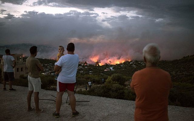 La gente mira un incendio forestal en la ciudad de Rafina, cerca de Atenas, Grecia, el 23 de julio de 2018. (ANGELOS TZORTZINIS / AFP)