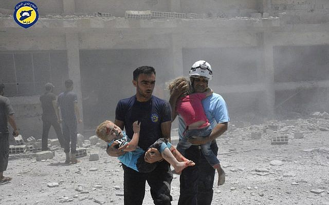 Los trabajadores de defensa civil conocidos como Cascos Blancos que llevan niños después de ataques aéreos golpean una escuela que alberga a varias personas desplazadas, en la parte occidental de la provincia meridional de Daraa, Siria, el 14 de junio de 2017. (Cascos blancos de Defensa Civil sirios a través de AP