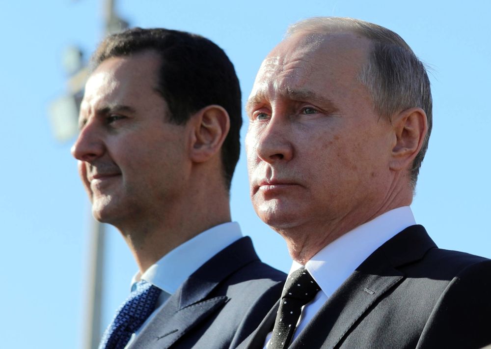 El presidente ruso, Vladimir Putin, a la derecha, y el presidente sirio, Bashar Assad, observan cómo las tropas marchan en la base aérea de Hemeimeem en Siria, el 11 de diciembre de 2017. (Mikhail Klimentyev, Sputnik, Kremlin Pool Photo via AP)