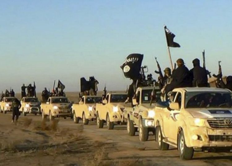 En esta foto sin fecha publicada por un sitio web militante, que se ha verificado y es coherente con otros informes de AP, los militantes del grupo Estado Islámico levantan sus armas y agitan banderas en sus vehículos, en un convoy en una carretera que conduce a Iraq, desde Raqqa, Siria. (Sitio web militante a través de AP)