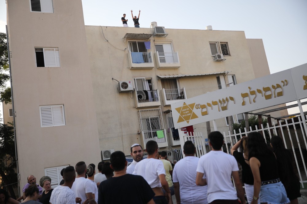 Personas en la escena en que un edificio fue alcanzado por un cohete en la ciudad de Sderot, en el sur de Israel, durante una escalada de disparos de cohetes desde Gaza sobre las ciudades israelíes, el 14 de julio de 2018. (Hadas Parush / Flash 90)