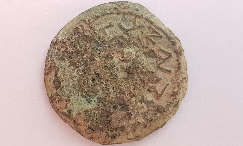 Una extraña moneda de bronce del año cuatro, acuñada en 69-70 EC durante la Gran Revuelta Judía, inscrita con 'Por la redención de Sión', fue descubierta en el tamizado húmedo de material de la ciudad de David, junio de 2018. (Ilan Shilmaiv / City de David)