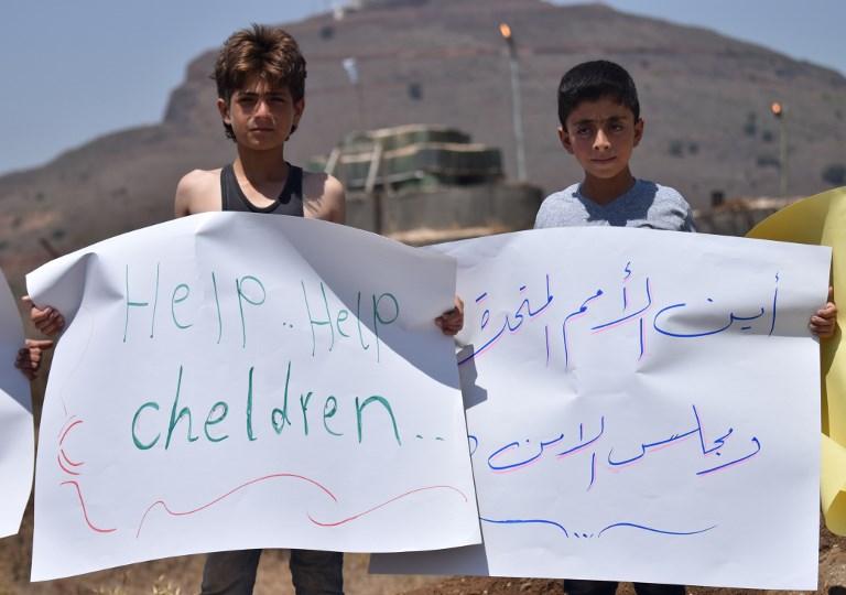 Niños sirios desplazados portan pancartas durante una protesta frente a una base de la ONU en la provincia de Quneitra, al sudoeste de Siria, cerca de la frontera con los Altos del Golán, exigiendo a las Naciones Unidas que ayuden a los desplazados varados en las fronteras entre Siria e Israel y Siria y Jordania el 4 de julio de 2018. (AFP / Mohamad Yusuf)