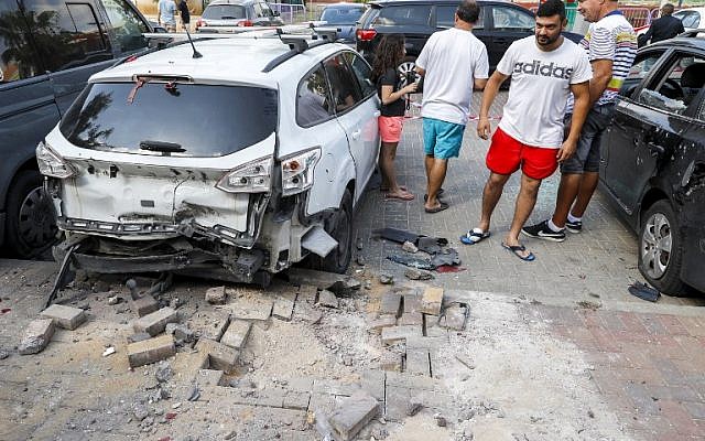 La gente se para junto a un automóvil que resultó dañado después de que un cohete disparado por terroristas de la Franja de Gaza cayó en la ciudad de Sderot, al sur de Israel, el 9 de agosto de 2018. (Jack Guez / AFP)