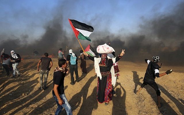 Los manifestantes palestinos arrojan piedras a las fuerzas israelíes mientras un hombre ondea la bandera nacional durante una manifestación en la frontera entre Israel y Gaza, al este de Khan Younis en el sur de la Franja de Gaza el 24 de agosto de 2018. (AFP PHOTO / SAID KHATIB)