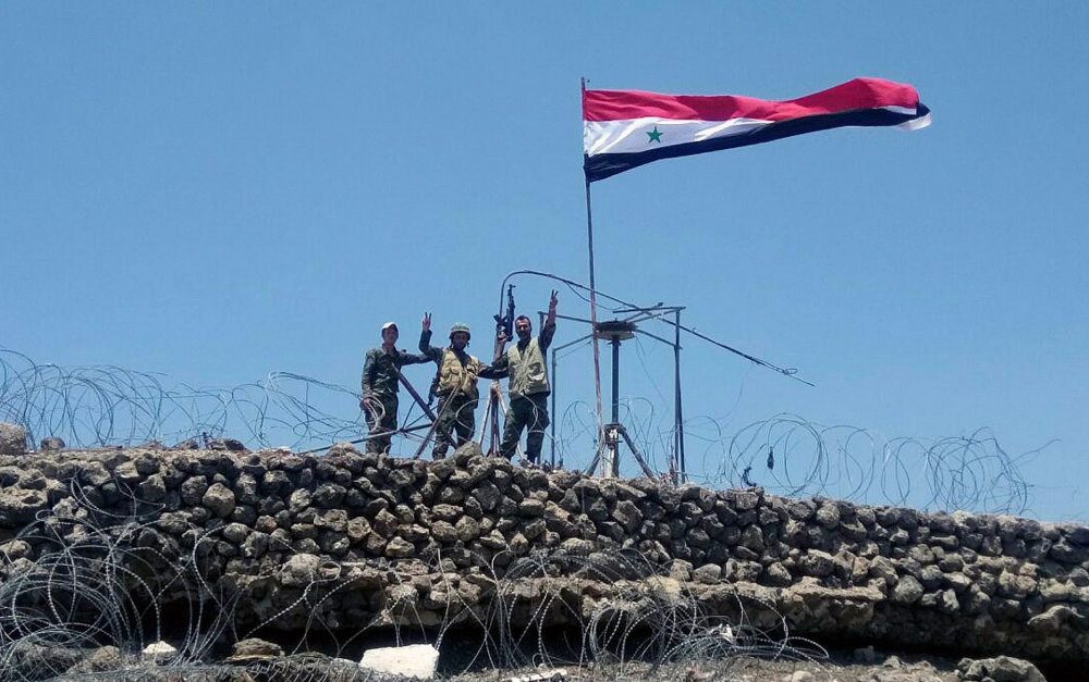 En este martes, 17 de julio de 2018, foto, publicada por la agencia oficial de noticias siria SANA, las tropas sirias muestran el letrero de la victoria junto a la bandera siria en Tell al-Haara, la colina más alta de la provincia suroccidental de Daraa, Siria. (SANA vía AP)