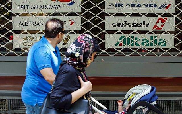 Una familia iraní pasa frente a la ventana cerrada de las oficinas cerradas de una agencia de viajes que muestra los logotipos de varias aerolíneas en la capital, Teherán, el 24 de agosto de 2018. (AFP Photo / Stringer)