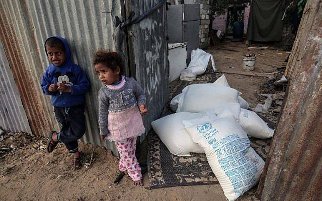 Niños palestinos se ponen de pie junto a bolsas de ayuda alimentaria proporcionadas por la agencia de la ONU para refugiados palestinos en el campo de refugiados de Rafah en el sur de la Franja de Gaza el 24 de enero de 2018. (AFP Photo / Said Khatib)