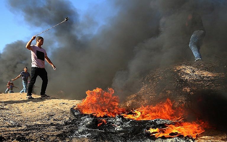 Un palestino usa un tirachinas junto a la quema de neumáticos durante los ataques en la frontera, al este de Khan Yunis en el sur de la Franja de Gaza el 10 de agosto de 2018. (AFP Photo / Said Khatib)