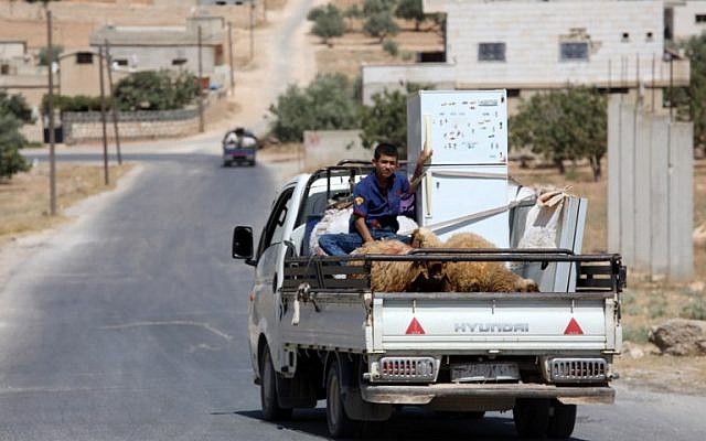 Un joven sirio montado en la parte trasera de un camión con ovejas y una nevera, el 6 de septiembre de 2018, huyendo del bombardeo de las fuerzas gubernamentales en la ciudad de al-Tamanah, en los límites meridionales de la provincia rebelde de Idlib. (AFP Photo / Omar Haj Kadour)