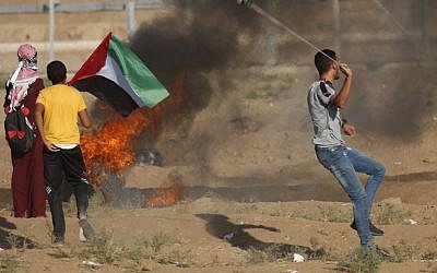 Un palestino usa un tirachinas mientras otros permanecen junto a un neumático en llamas y agitan una bandera nacional durante un ataque a lo largo de la valla fronteriza al este de la ciudad de Gaza el 14 de septiembre de 2018. (AFP PHOTO / Said KHATIB)