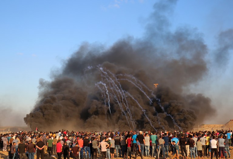 Los manifestantes palestinos observan cómo las latas de gas lacrimógeno disparadas por las fuerzas israelíes se filtran a través del humo negro de las llantas incendiadas durante una manifestación a lo largo de la valla fronteriza al este de la ciudad de Gaza el 14 de septiembre de 2018. (AFP PHOTO / SAID KHATIB)