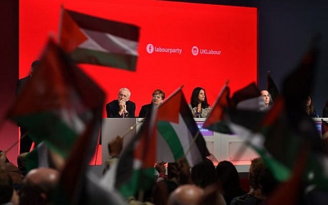 Los delegados en la conferencia del Partido Laborista en Liverpool sostienen banderas palestinas durante un debate el 25 de septiembre de 2018, mientras el líder Jeremy Corbyn observa desde el podio. (AFP Photo / Oli Scarff)