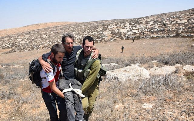 Un activista de izquierda herido siendo escoltado por otro activista y un soldado de las FDI después de ser presuntamente atacado por colonos, cerca del asentamiento de Mitzpeh Yair en Cisjordania, el 25 de agosto de 2108. (B'Tselem)