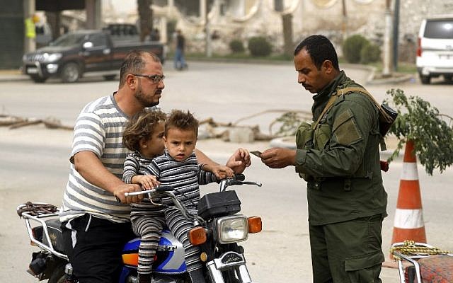 Un miembro de las fuerzas de seguridad locales del consejo civil de Raqqa verifica los documentos de identificación de un hombre que viajaba en una motocicleta con dos niños en un puesto de control que aseguraba la entrada de vehículos a la ciudad del este de Siria y al antiguo bastión del Estado Islámico (IS), el 16 de octubre de 2018. ( Delil Souleiman / AFP)