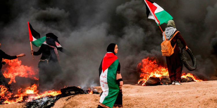 mujeres palestinas portan y visten banderas palestinas mientras se encuentran en medio del humo de los neumáticos quemados durante los ataques cerca de la frontera con Israel al este de la ciudad de Gaza el 26 de octubre de 2018 AFP