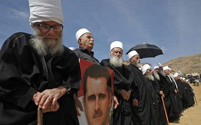 Los miembros ancianos de la comunidad drusa sostienen un retrato del presidente sirio Bashar Assad durante un mitin en la aldea drusa de Majdal Shams en los Altos del Golán de Israel, el 6 de octubre de 2018, en conmemoración del 45 aniversario de la guerra árabe-israelí de 1973. (AFP PHOTO / JALAA MAREY)