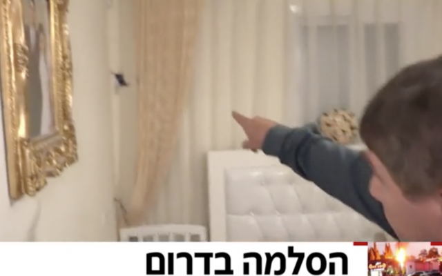 El reportero de Hadashot TV Moshe Nussbaum muestra dónde un trozo de metralla de un cohete de Hamás atravesó la pared de una casa en Netivot, 12 de noviembre de 2018 (noticias de Hadashot TV)
