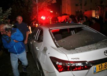 Dos hombres pasan por delante de un vehículo que fue alcanzado por un cohete disparado desde la Franja de Gaza, en la ciudad de Ashkelon, al sur de Israel, el 12 de noviembre de 2018. (GIL COHEN-MAGEN / AFP)