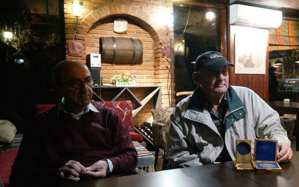 Rexhep Hoxha, izquierda, y Fatos Qoqja en un bar en Tirania, Albania, el 8 de noviembre de 2017. Qoqja aparece con una medalla que recibió su padre por salvar a judíos durante el Holocausto. (Cnaan Liphshiz / via JTA)