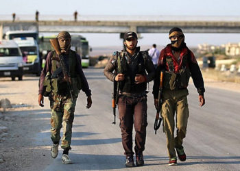 Los combatientes rebeldes sirios de la provincia de Quneitra caminan con sus rifles mientras esperan en el punto de cruce de Morek para ser transferidos a las provincias de Idlib y Alepo el 21 de julio de 2018. (AFP Photo / Aaref Watad)