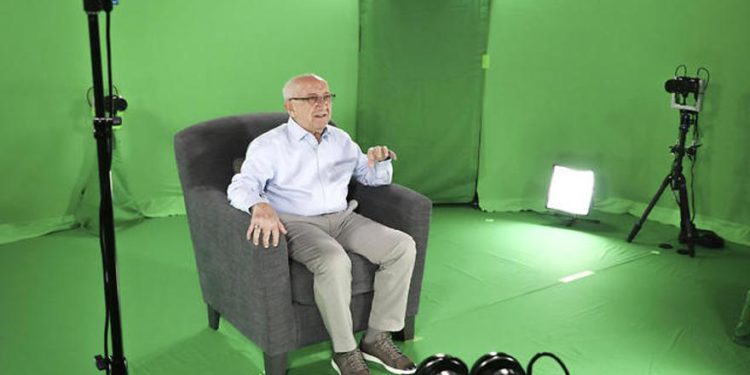 El sobreviviente del holocausto Max Glauben sentado en una sala de pantalla verde interactiva mientras filma una pieza para