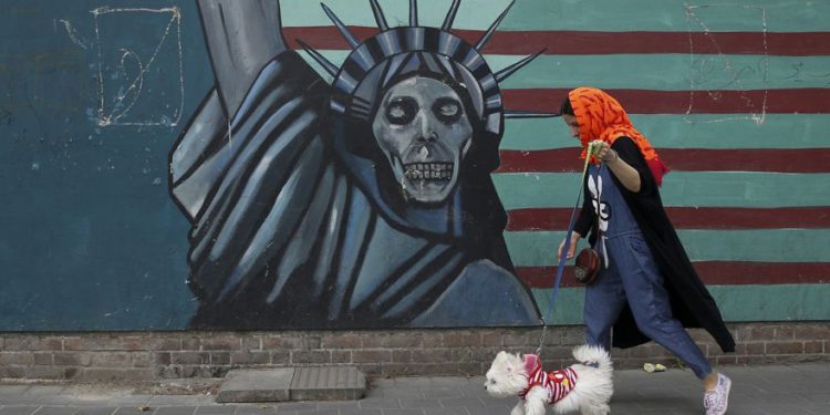 Una mujer pasea a su perro ante un mural antiestadounidense pintado en la pared de la antigua Embajada de los Estados Unidos en Teherán, mayo de 2018 (Foto AP / Vahid Salemi)