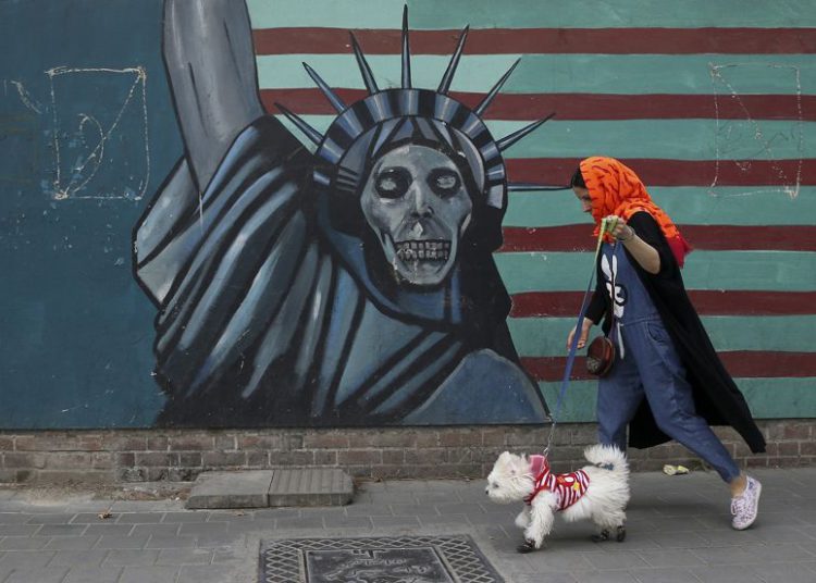 Una mujer pasea a su perro ante un mural antiestadounidense pintado en la pared de la antigua Embajada de los Estados Unidos en Teherán, mayo de 2018 (Foto AP / Vahid Salemi)