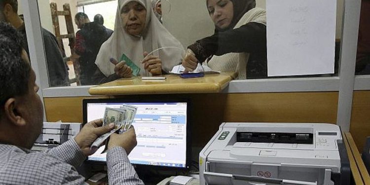 Un empleado del gobierno designado por Hamas en Gaza firma un documento para recibir el 50 por ciento de su salario atrasado de los fondos donados por Qatar, mientras que otros esperan en la cola, en la oficina principal de correos de Gaza, en la ciudad de Gaza, el 7 de diciembre de 2018. (Foto AP / Adel Hana)