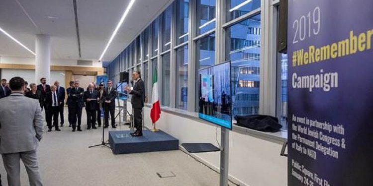 El embajador italiano ante la OTAN, Claudio Bisogniero, habla en la sede de la OTAN junto a una pantalla que proyecta la foto del #Recordamos la transmisión en vivo desde Auschwitz-Birkenau. Crédito: OTAN.