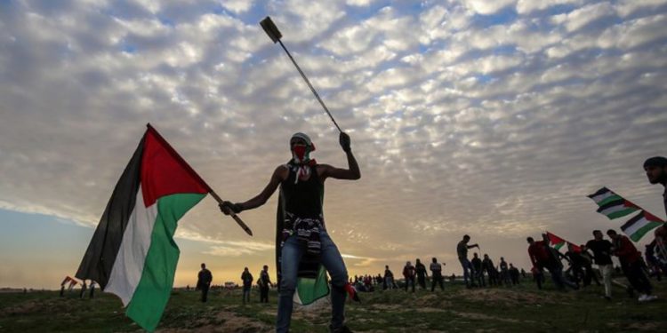 Un manifestante palestino porta una bandera nacional y una honda durante una manifestación cerca de la cerca a lo largo de la frontera con Israel, al este de la ciudad de Gaza, el 1 de febrero de 2019. (Dijo KHATIB / AFP)