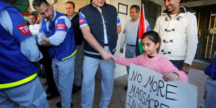 Una niña palestina le da la mano a un miembro de la Presencia Internacional Temporal en Hebrón (TIPH) en el lado palestino H1 de la ciudad durante una protesta contra la decisión de Israel de no renovar su mandato, 30 de enero de 2019. (Crédito de la foto: MUSSA QAWASMA / REUTERS)